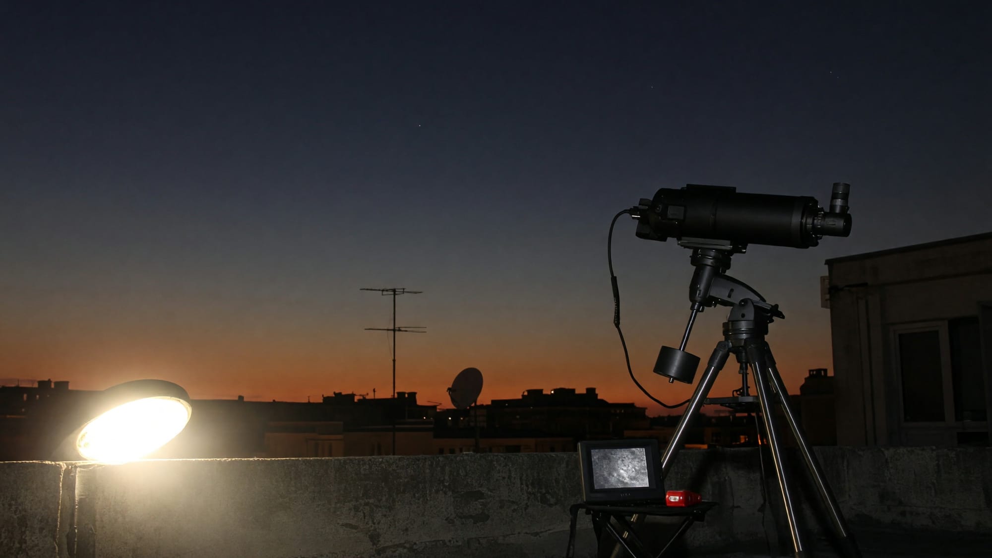 A streetlight flaring behind a concrete parapet with a telescope in silhouette