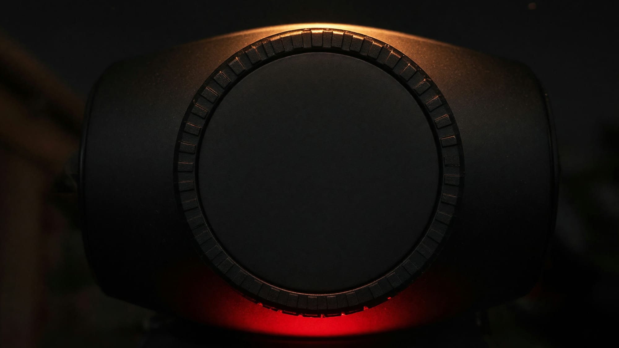 The front of a telescope tube with its lens cap fitted, rim-lit against the dark
